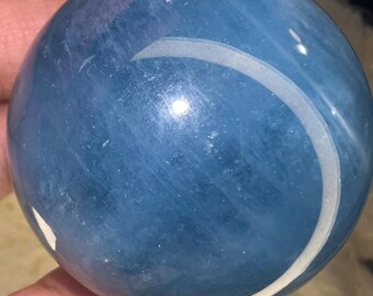 Puede incluir: Una esfera lisa, azul y blanca con un patrón de remolino. La esfera está hecha de piedra pulida y tiene un acabado brillante.