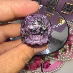 May include: Purple and black carved stone dragon figurine. The dragon has a detailed face and is made of a smooth, polished stone.