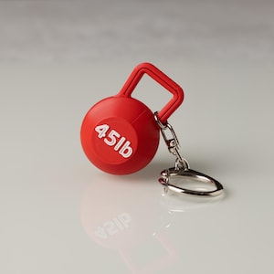 Könnte beinhalten: Roter 45lb Kettlebell-Schlüsselanhänger. Der Schlüsselanhänger ist aus Kunststoff und hat einen silbernen Metallring.