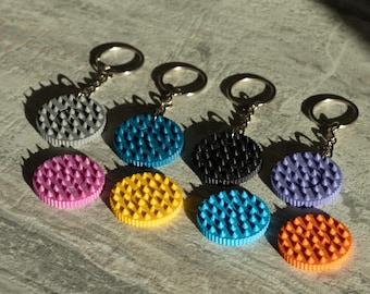 May include: A collection of colorful keychains with textured, circular pendants. The keychains feature a variety of colors, including pink, yellow, blue, black, purple, gray, and orange. Each keychain has a silver-colored ring.