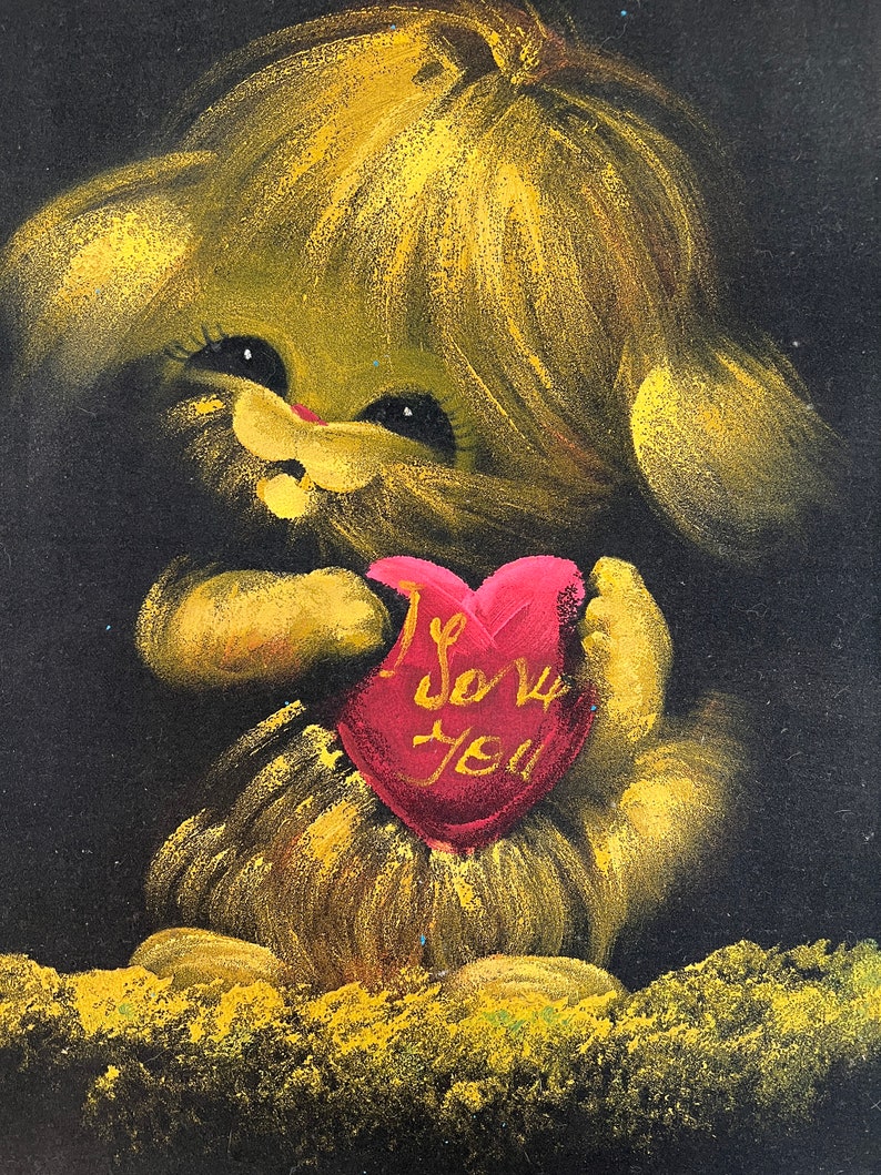 Puede incluir: Un animal amarillo y peludo con ojos grandes sostiene un coraz&oacute;n rojo que dice "Te amo". El animal est&aacute; sobre un fondo negro.