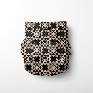 May include: A beige and black patterned cloth nappy with a geometric design. The nappy has multiple poppers for adjusting the fit.