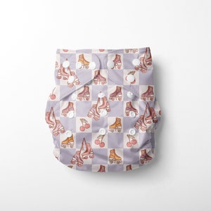 May include: A reusable cloth nappy featuring a repeating pattern of roller skates and cherries on a lilac and white checkered background. It has snap closures.