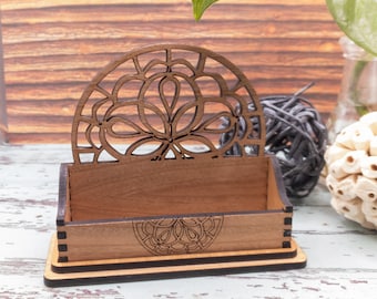 Puede incluir: Un porta tarjetas de visita de madera con un diseño decorativo cortado con láser. El porta tarjetas tiene un acabado marrón oscuro y una base negra.