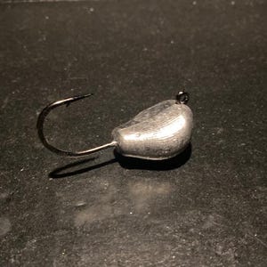 May include: A silver fishing jig with a hook and a round, teardrop-shaped weight.