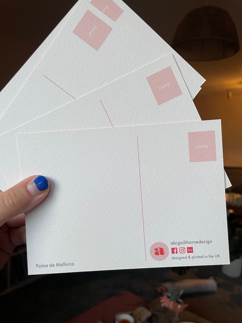 May include: A white postcard with a pink stamp area and the text "Palma de Mallorca". The postcard has a logo with the letter "a" and the text "abigailthornedesign" with social media icons for Facebook, Instagram, and Etsy. The text "designed & printed in the UK" is also included.