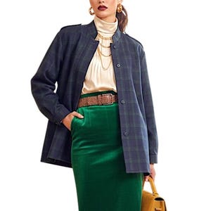 May include: A dark blue plaid jacket with a button-front closure, worn over a cream-coloured mock neck top. The outfit includes a vibrant green midi skirt cinched with a textured brown belt and layered gold chain necklaces, paired with a mustard bag.