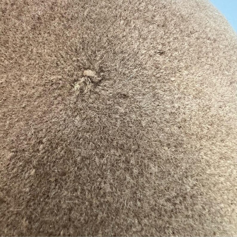 Pode incluir: Close-up de um tecido bege texturizado. O tecido tem uma apar&ecirc;ncia ligeiramente &aacute;spera e feltrada, com uma pequena &aacute;rea elevada no centro. A cor &eacute; um tom neutro e suave, adequado para v&aacute;rias aplica&ccedil;&otilde;es.