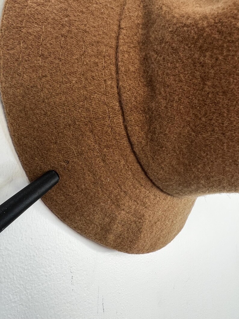 Pode incluir: Um close-up de um chap&eacute;u de l&atilde; castanho. O chap&eacute;u tem uma copa arredondada e uma aba. O chap&eacute;u &eacute; feito de um material macio e texturizado. O chap&eacute;u &eacute; de uma cor quente e neutra.