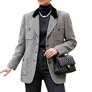 Puede incluir: Un blazer cruzado de pata de gallo en blanco y negro con cuello de terciopelo negro, combinado con una blusa de cuello alto negra y jeans oscuros. Un bolso negro acolchado con cierre dorado y correa de cadena colgado al hombro.