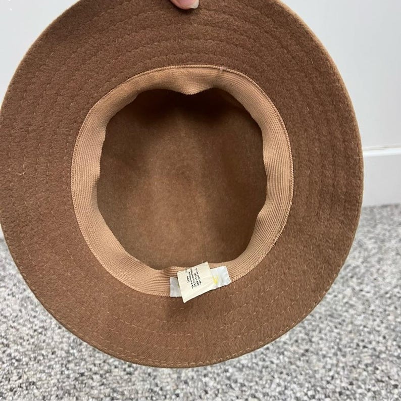 Pode incluir: Chap&eacute;u de l&atilde; castanho com copa arredondada e aba larga. O interior apresenta um forro bege e uma etiqueta. O chap&eacute;u &eacute; de cor neutra e adequado para v&aacute;rias roupas.