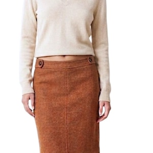 Puede incluir: Un su&eacute;ter beige de manga larga con cuello en V combinado con una falda a la rodilla de textura color &oacute;xido. La falda presenta una silueta recta, una costura central vertical y dos botones decorativos marrones en la cintura.