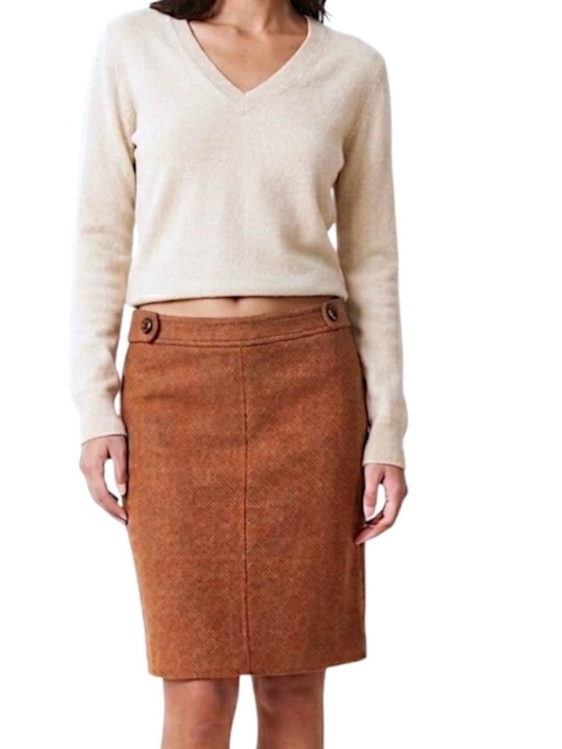 Puede incluir: Un su&eacute;ter beige de manga larga con cuello en V combinado con una falda a la rodilla de textura color &oacute;xido. La falda presenta una silueta recta, una costura central vertical y dos botones decorativos marrones en la cintura.