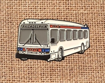 May include: A white and black enamel pin of a Philadelphia SEPTA bus. The bus has the word "PHILADELPHIA" above the front window and "SEPTA" on the front and side. The bus has red and blue accents.