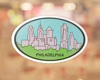 May include: An oval sticker featuring a stylized Philadelphia skyline in shades of gray and white against a light blue background. The city's name is printed in black at the bottom, with a green border.