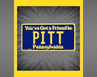 May include: A blue and yellow enamel pin shaped like a license plate with the text "You've Got a Friend in PITT Pennsylvania".