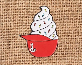 May include: A red baseball cap pin with a white soft serve ice cream design. The ice cream has colorful sprinkles. The pin is a fun accessory for hats, bags, or jackets.