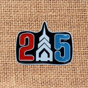 May include: A black and white enamel pin with the numbers "2" in red and "5" in blue. The numbers are outlined in white and black. The pin also features a white architectural design.