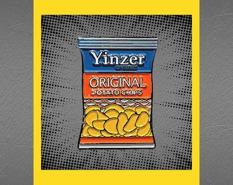 May include: A blue and orange enamel pin shaped like a bag of potato chips. The bag says "Yinzter of Burgh Original Potato Chips".