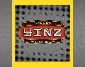 May include: Red and white enamel pin with the text "MADE IN YINZ PITTSBURGH" in a black and gold frame. The pin is on a gray background with a black and white polka dot pattern.