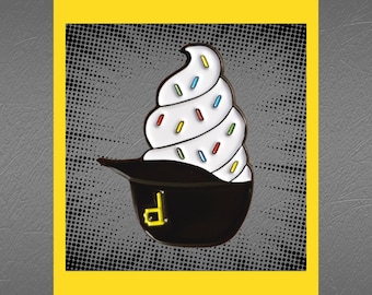 May include: A white and black enamel pin featuring a swirl of white frosting with colorful sprinkles, topped with a black hat with a white letter 'D' on the front. The pin is set against a black and white polka dot background.