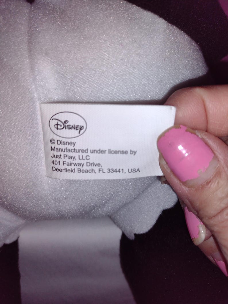 Op de afbeelding: Wit etiket met zwarte tekst die luidt: "Disney &copy;Disney Gemaakt onder licentie van Just Play, LLC 401 Fairway Drive, Deerfield Beach, FL 33441, USA"