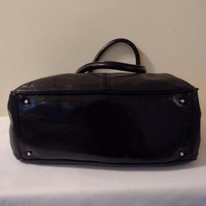 Op de afbeelding: Zwarte leren handtas met een glanzende afwerking. De tas heeft twee handvatten en een ritssluiting.