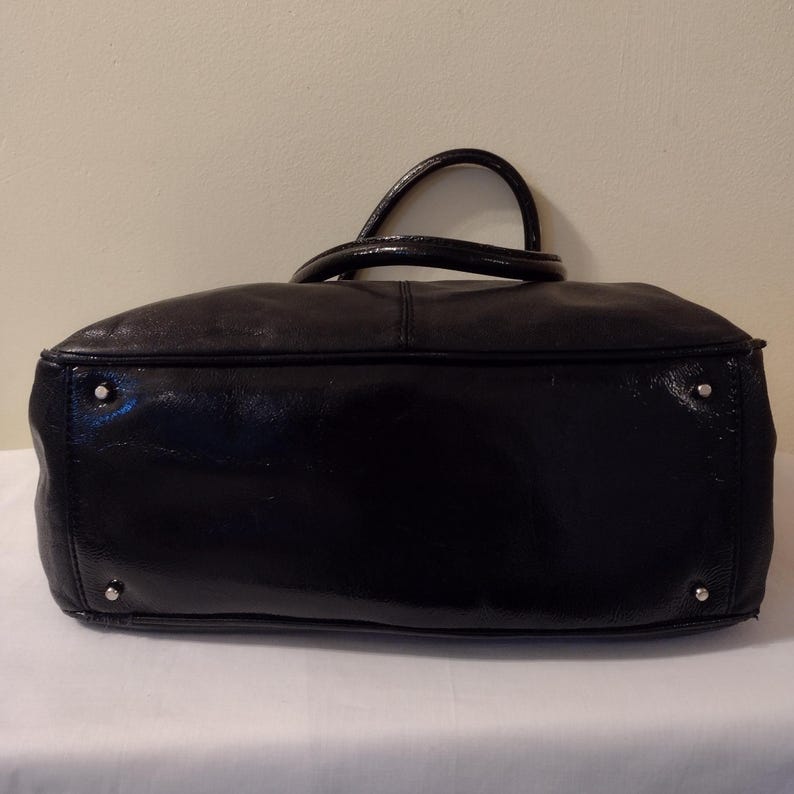 Op de afbeelding: Zwarte leren handtas met een glanzende afwerking. De tas heeft twee handvatten en een ritssluiting.