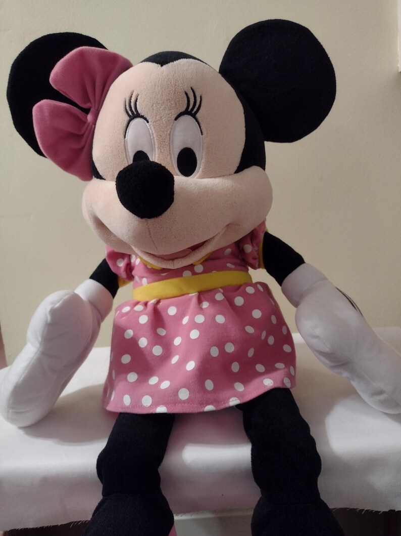 Op de afbeelding: Een groot pluche speelgoed van Minnie Mouse, die een roze gebloemde jurk draagt met een gele riem en een roze strik.