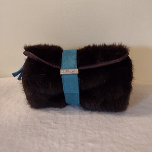 May include: A brown fur clutch with a teal blue suede strap and a gold clasp with rhinestones.