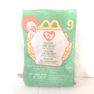 May include: A green and white Ty Beanie Baby packaging with a picture of Ronald McDonald. The packaging is for Claude the Crab, a plush toy. The packaging says "Licensed for distribution only by McDonald's restaurants with food purchase. Not for resale."