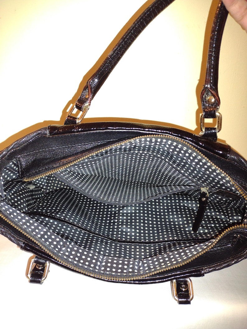 Op de afbeelding: Zwarte leren tote bag met een witte stippenvoering. De tas heeft twee bovenste handvatten en een ritssluiting.
