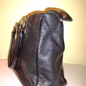 Op de afbeelding: Zwarte leren handtas met een gouden rits en handvat. De tas heeft een gestructureerde vorm en een gladde afwerking.