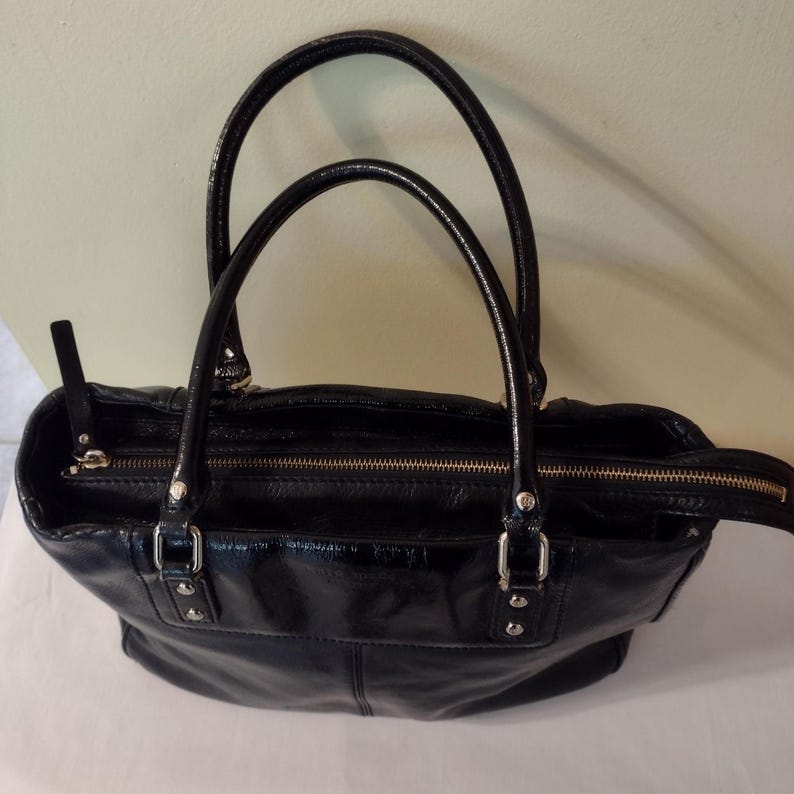 Op de afbeelding: Een zwarte leren tote bag met een ritssluiting en twee handvatten.