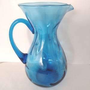 May include: A blue glass jug with a wide mouth and a handle. The jug has a textured, wavy design.