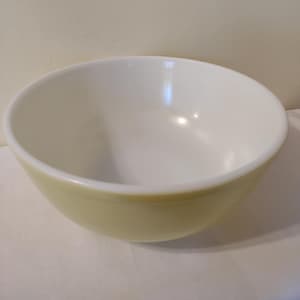 Puede incluir: Un tazón mezclador vintage amarillo con un interior blanco. El tazón está hecho de vidrio y tiene una forma redonda y lisa.