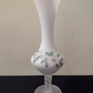 May include: A white frosted glass vase with a floral design. The vase has a twisted stem and a round base.