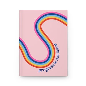 May include: A pink notebook with a rainbow design and the text "progress is not linear" in blue.