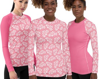 May include: Three long-sleeved rash guards. One is solid pink, and the other two are pink with white floral patterns. The solid pink rash guard has pink sleeves. All three are worn with black bottoms.