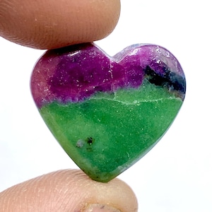 Może przedstawiać: Wisiorek w kształcie serca z zielonego i fioletowego kamienia szlachetnego. Kamień ma naturalną, szorstką fakturę i jest żywym odcieniem zieleni z fioletowym pasem u góry.