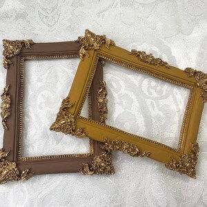 以下が含まれることがあります： 白い背景に、装飾的なフレームが2つ。1つは茶色、もう1つは金色で、複雑な模様が施されています。