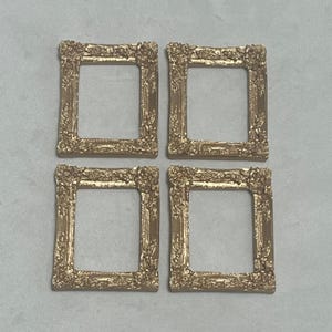 May include: Set of four gold-toned picture frames with ornate detailing. Each frame has a square shape and a simple, clean design.