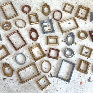 May include: A collection of small, decorative picture frames in various shapes, including rectangular, square, and oval. The frames feature metallic finishes in gold, silver, copper, and bronze tones, with some containing pressed botanical elements.