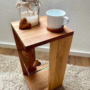 Könnte beinhalten: Ein Beistelltisch aus Holz mit natürlicher Oberfläche, mit einem Glasregal und zwei geschnitzten Holzherzen. Eine weiße Tasse auf einem Untersetzer aus Kork, ein Glas und ein Holzherz befinden sich auf der Tischplatte. Der Tisch steht auf einem hellen Teppich.