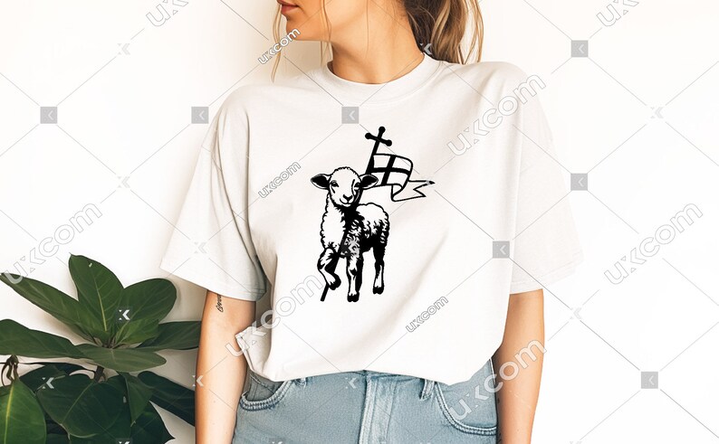 May include: White t-shirt with a black and white graphic of a lamb carrying a cross and a flag. The lamb is standing on a stick.