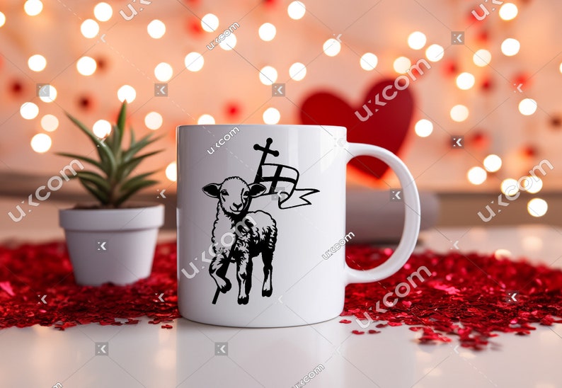 May include: White ceramic mug with a black and white illustration of a lamb carrying a cross. The mug is on a red heart-shaped confetti background.