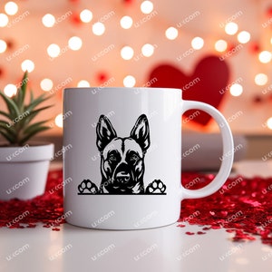 May include: White ceramic mug featuring a black silhouette of a dog's face and paws. The dog's head is centered on the mug, with its ears perked up. The mug has a curved handle and is set against a blurred background.