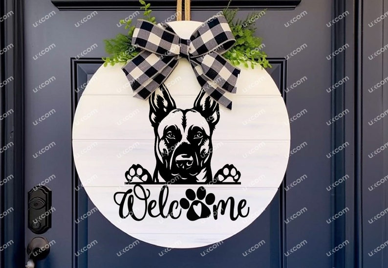 May include: A round, white wooden welcome sign featuring a black and white dog graphic. The sign has a black and white buffalo check bow and greenery at the top. The word "Welcome" is written in script below the dog.