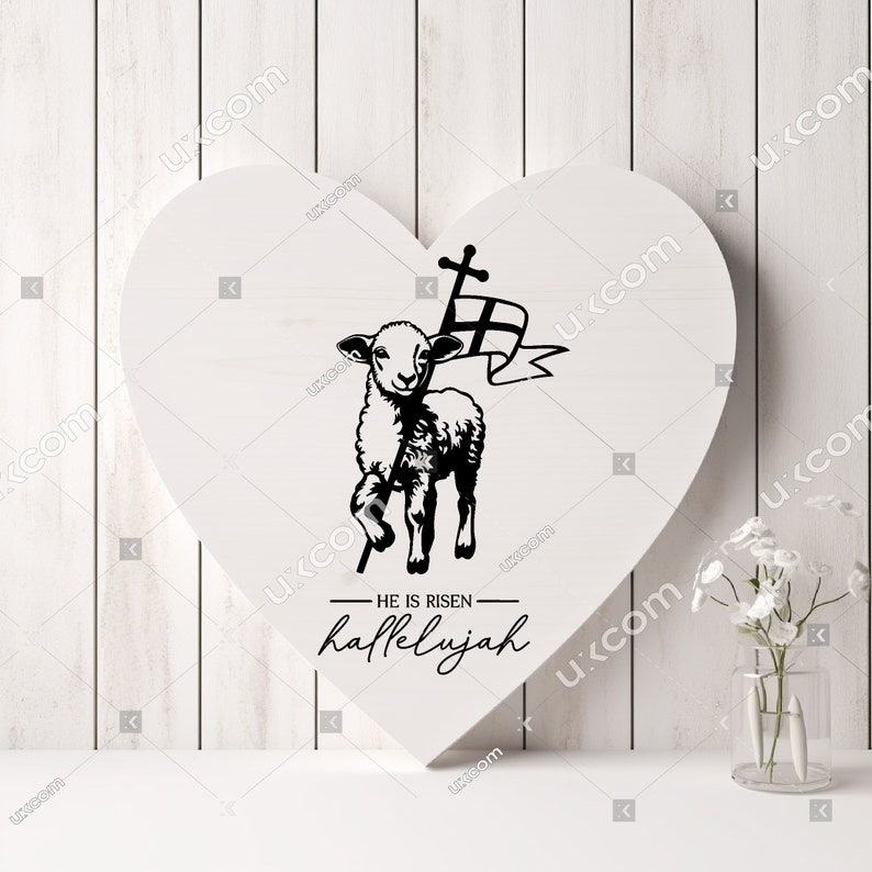 May include: A white heart-shaped wooden sign with a black silhouette of a lamb carrying a cross and a banner. The text "HE IS RISEN - hallelujah" is written below the lamb.