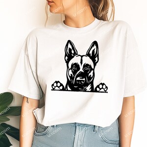 May include: A white t-shirt featuring a black and white graphic of a dog's face and paws. The dog's head is centered, with its ears perked up. The paws are at the bottom of the graphic, giving the impression the dog is peeking over.